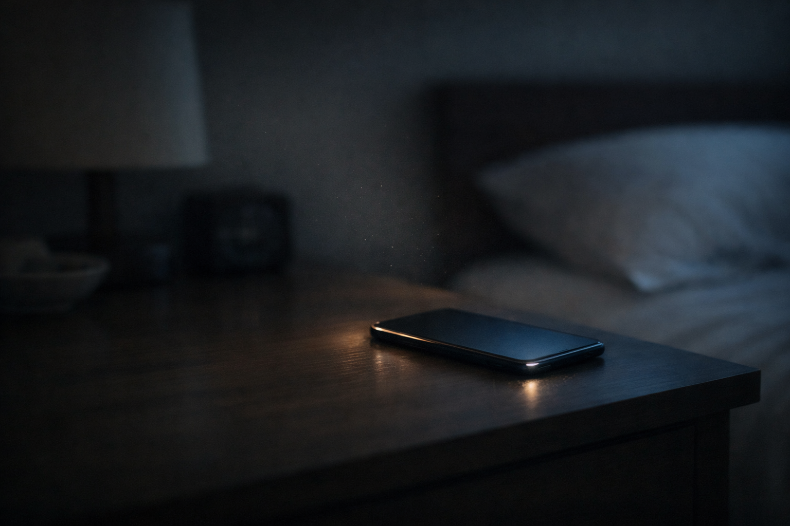 薄暗い部屋のナイトテーブルで、伏せたスマホが縁からほのかに光っている