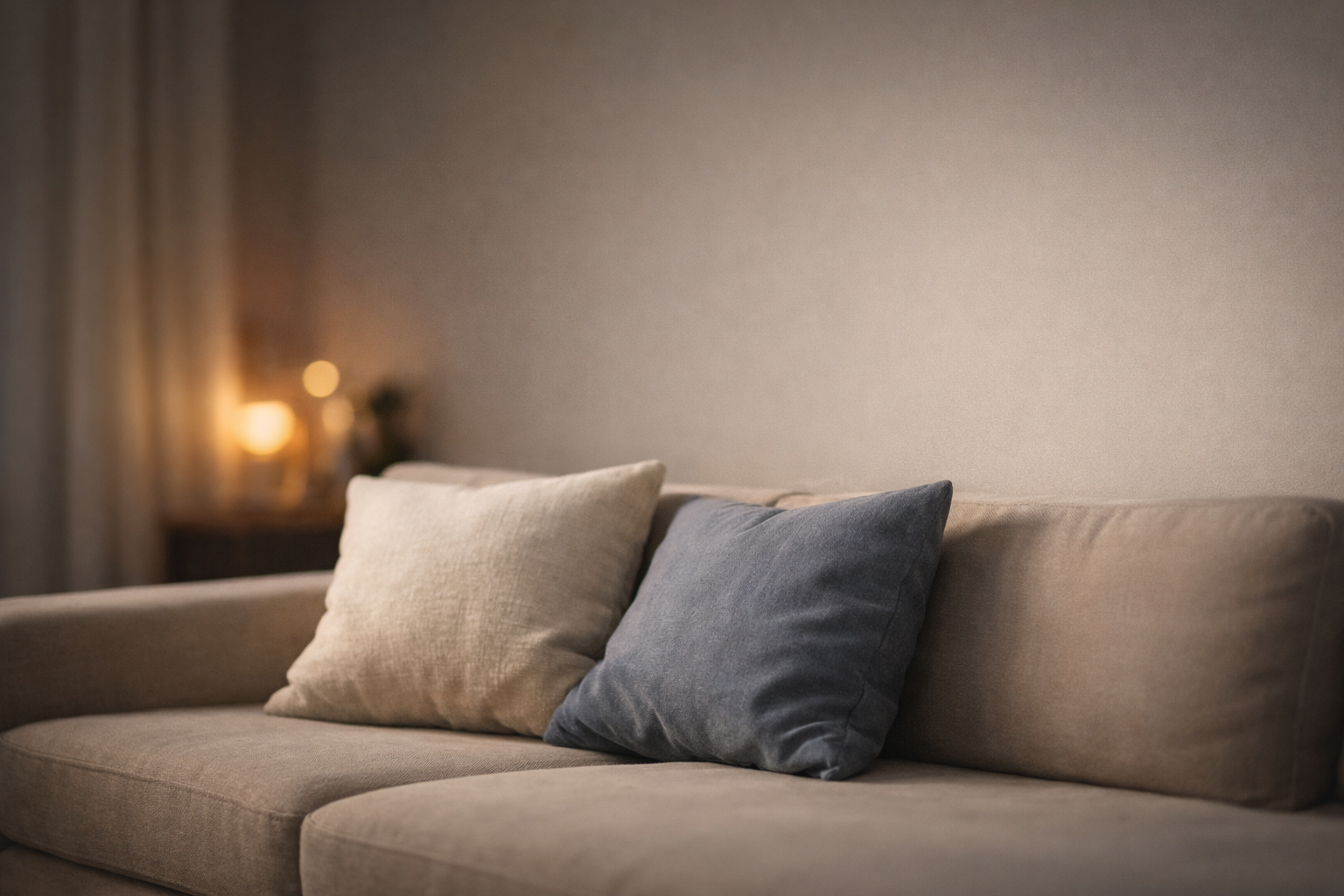 夕方のリビングのソファと、寄り添う2つのクッション（やわらかな灯り）